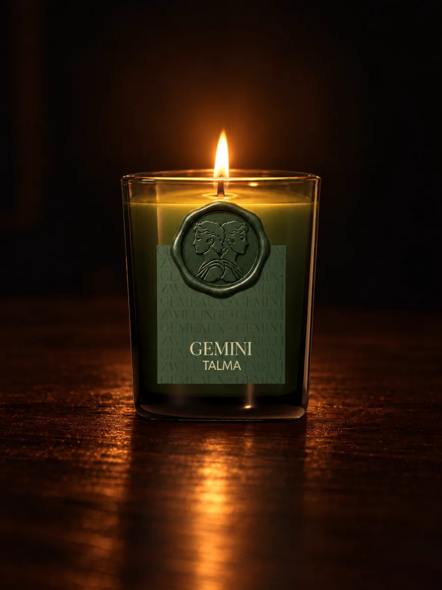 The Gemini candle lit in the dark, its wax seal on the green glass.