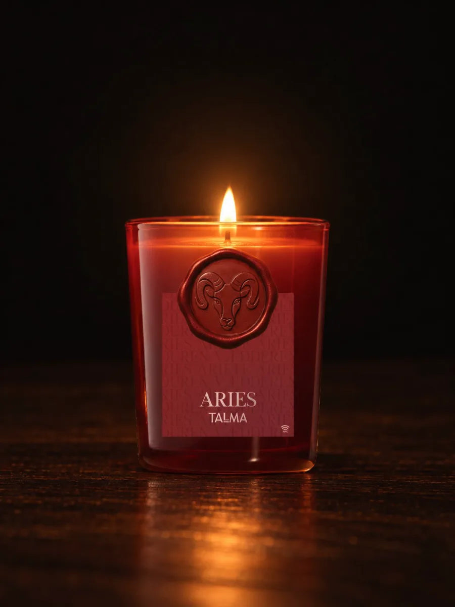 The Aries candle lit in the dark, its wax seal on the red glass.